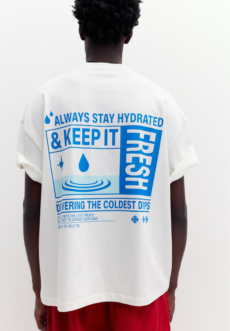 Personne à la peau foncée et aux cheveux bouclés porte un T-shirt blanc avec un texte bleu sur l'importance de rester hydraté et de rester frais.