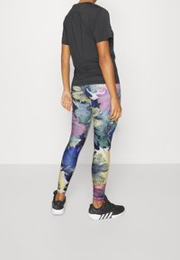 Maglietta nera a maniche corte abbinata a leggings stampati floreali colorati che presentano tonalità di viola, blu e giallo. Scarpe da ginnastica nere con dettagli bianchi.