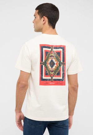 Cream t-shirt featuring a geometric, multicolored pattern on the back in red, navy, green, and beige, crafted from soft cotton fabric.