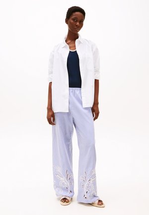 Cămașă albă cu butoni, purtata peste un top navy, asociată cu pantaloni largi rayurați în nuanțe de albastru deschis, cu accente de broderie albă la tiv.