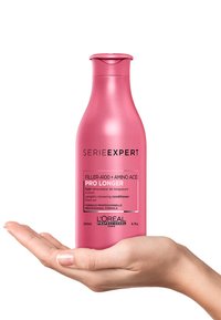 Roze plastic fles van L'Oréal Serie Expert Pro Longer conditioner, met een slank ontwerp, schroefdop en zwarte tekst op een witte label, vastgehouden in een hand.