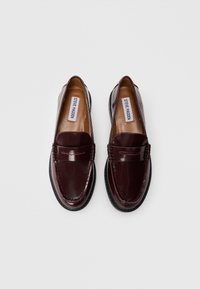 Burgundy leather loafers with a smooth finish, featuring a stitched seam, flat sole, and a small cutout design on the upper.