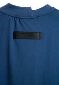 Prenda de tela azul con cuello acanalado y una etiqueta rectangular negra cosida cerca del escote.