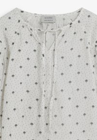 Blusa blanca con estampado de árboles negros, con escote en V y cierre de lazo. Fabricada con tela ligera y mangas fruncidas para un ajuste suelto.