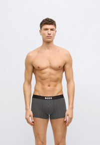 Fekete boxeralsó fehér pöttyös mintával, szilárd fekete derékrésszel, amelyen "BOSS" logó található. Az anyag simának és rugalmasnak tűnik.