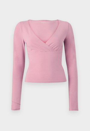 Soft pink long-sleeve wrap-style fitted top with V-neck and slightly cropped hem against a white background.