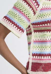 Háčkovaný krátky rukáv s horizontálnymi pruhmi v krémovej, bordovej, ružovej, zelenej a svetlomodrej farbe na ramene a trupe osoby.