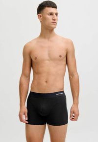 Black boxer briefs with a soft texture and elastic waistband. Features logo on the band, fitted design, and mid-thigh length.