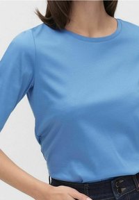 Světle modré tričko s krátkým rukávem vyrobené z měkké bavlněné tkaniny, s kulatým výstřihem a hladkým povrchem, v kombinaci s tmavými džíny z denimu se zdobením na knoflíky.