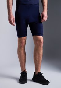Calções de ciclismo azul marinho com um design ajustado, cintura elástica e área de assento almofadada, combinados com sapatos de corrida pretos.