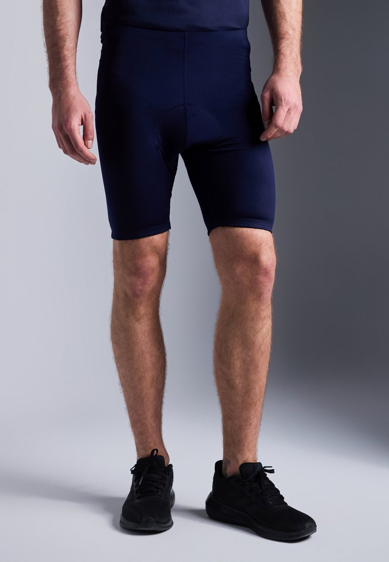 Calções de ciclismo azul marinho com um design ajustado, cintura elástica e área de assento almofadada, combinados com sapatos de corrida pretos.