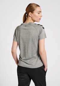 Grå atletisk t-shirt med korte ærmer, rund hals og sorte accentmønstre på skuldrene. Glat tekstur og tætsiddende design.