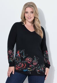 Czarna koszula z długim rękawem ozdobiona wielokolorowym kwiatowym haftem wzdłuż rękawów i dolnego brzegu; dekolt w kształcie litery V, gładka faktura tkaniny.