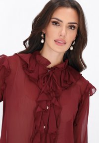 Bordó chiffon blúz fodros gallérral és elülső gombolattal, díszgombokkal és hosszú, fodros mandzsettás ujjakkal.