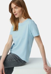 Lichtblauw katoenen t-shirt met korte mouwen en een ronde hals. De stof is glad met een relaxed fit. Gecombineerd met grijze jeans.