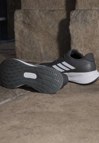 Chaussures de sport noires et blanches avec semelles texturées placées sur une surface en pierre près d'un mur en pierre en arrière-plan.