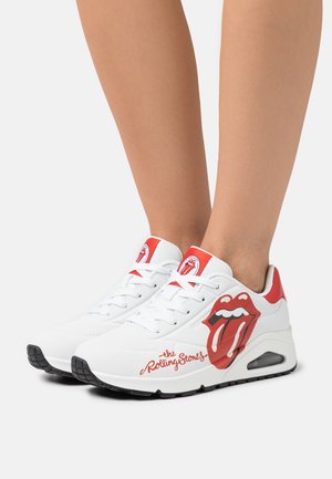 Baskets blanches avec des accents rouges, arborant un logo emblématique de la langue des Rolling Stones sur le côté et le nom de la marque imprimé en rouge.