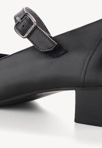 Chaussure Mary Jane en cuir noir avec un petit talon bloc et une bride réglable à boucle argentée sur le cou-de-pied.