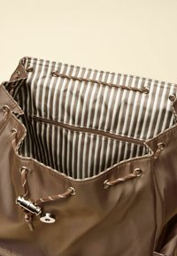 Rjava satenasta torbica z vrvico, okrašena z metalnimi poudarki; podložena z rjavim in belim črtastim vzorcem; vsebuje notranji žep z zadrgo.