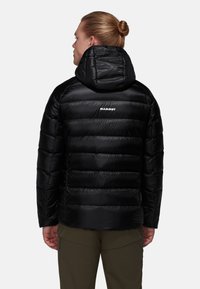 Svart puffjacka med huva, med en kviltad design och slät textur. "MAMMUT"-logga visad på ovandelen av ryggen.