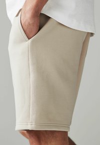 Shorts en coton beige avec une coupe ajustée, dotés de poches latérales et d'une texture lisse. Bord ourlé avec des détails de couture visibles.