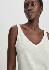 Vaaleanharmaa hihaton paita, jossa on V-pääntie, pehmeä tekstuuri ja leveät olkaimet. Paitaa korostaa valkoinen trimmi pääntien ympärillä.