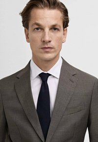 Gray suit with a textured fabric, white dress shirt, and navy tie. The jacket features a single pocket and notch lapels. Smooth, tailored fit.