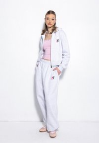 Jasnoszara bluza z kapturem i dresy wykonane z miękkiego materiału, z małym różowo-czarnym logo na klatce piersiowej i lewej nodze spodni.