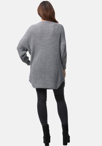 Maglione grigio a maniche lunghe in maglia con una vestibilità ampia, tessuto strutturato, spacchi laterali e orlo arrotondato, abbinato a jeans skinny neri e stivali alla caviglia.