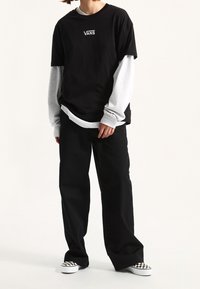 Black Vans t-shirt layered over a gray long-sleeve shirt, paired with black wide-leg pants and black-and-white checkered slip-on shoes.