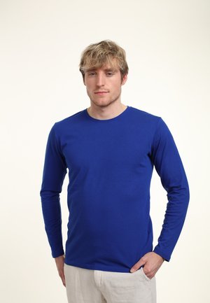 Langetermijnshirt van helderblauwe katoen met een ronde halslijn en een aansluitend ontwerp, gedragen met lichte broek.