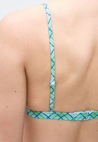 Ώμος και άνω μέρος της πλάτης ενός ατόμου που φοράει μπλε-πράσινο καρό σουτιέν με ρυθμιζόμενους ιμάντες και κούμπωμα στο πίσω μέρος.