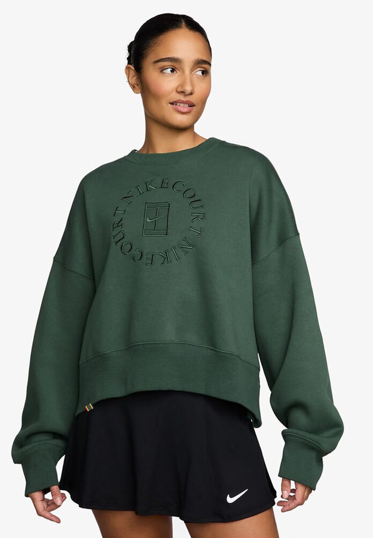 Sudadera verde con cuello redondo, corte holgado y un diseño de logo texturizado. Combinada con una falda deportiva negra que cuenta con un logo blanco.