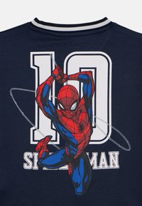 Marineblå t-skjorte med et Spider-Man-grafikk, tallet "10" i hvitt, og et teksturert, pustende stoff for komfort.