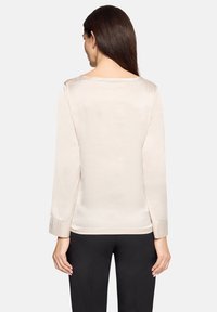 Langärmlige, beigefarbene Satinbluse mit rundem Ausschnitt und glatter Textur. Mit eng anliegenden Manschetten; Rückansicht zeigt schlichtes Design und Eleganz.