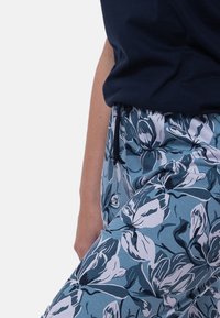 Housut, joissa on kukkakuosi sinisen ja valkoisen sävyissä, joustovyötäröllä ja kevyestä kankaasta. Designissa on suuria, tyyliteltyjä kukkia.