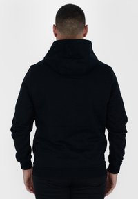 Felpa nera con vestibilità rilassata, dotata di cappuccio con coulisse, polsini a coste e una texture di tessuto liscia. Nessun logo o motivo visibile.