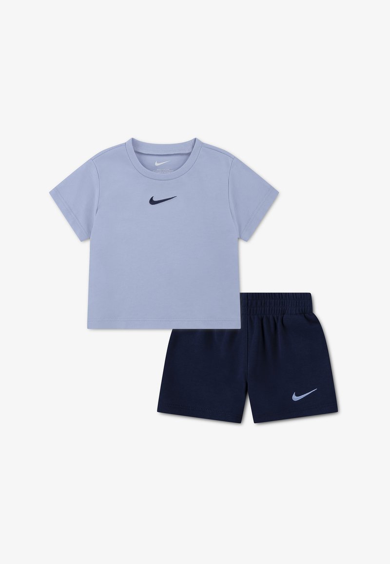 Φωτεινό γαλάζιο κοντομάνικο t-shirt της Nike και σκούρα μπλε σορτς με ελαστική μέση και λογότυπο της Nike στο στήθος και στο πόδι, σε λευκό φόντο.