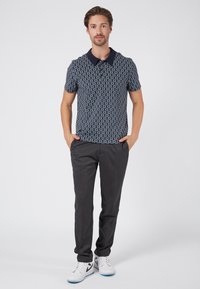 Marinblå kortärmad polo med ett geometriskt mönster, tillsammans med mörkgrå slim-fit byxor och vita träningsskor.