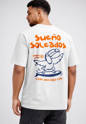 Man wearing white t-shirt with orange and blue toucan surfing graphic and text "Sueño soleados" and "Livin' the easy life" on back.