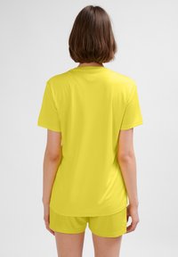 Żółta, krótka koszulka z miękkiego materiału, o luźnym kroju i gładkiej fakturze, noszona z dopasowanymi szortami.