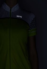 Maillot de ciclismo de manga corta en un brillante verde lima con una sección superior de puntos blancos y un logo reflectante de GORE; cuenta con un cierre frontal.