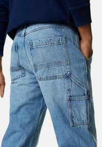 Pantalones de mezclilla azul claro con un ajuste relajado, múltiples bolsillos, detalles de costura y una ligera textura. La cintura es ligeramente visible.