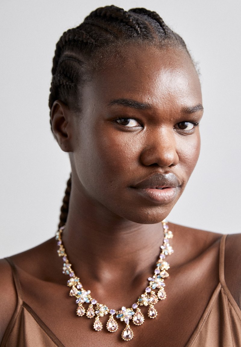 Multi-colored gemstone necklace with droplets, featuring gold accents and floral motifs, displayed against a neutral background.