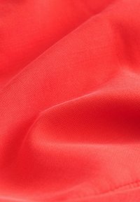 Tela de color rojo brillante con pliegues suaves que muestran una textura tejida fina y lisa y una costura sutil a lo largo del borde.