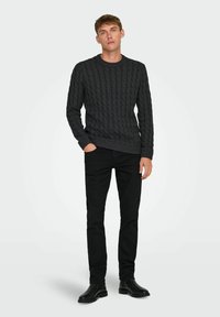 Suéter de punto cable en gris oscuro con cuello redondo, combinado con pantalones negros ajustados ybotines de cuero negro.