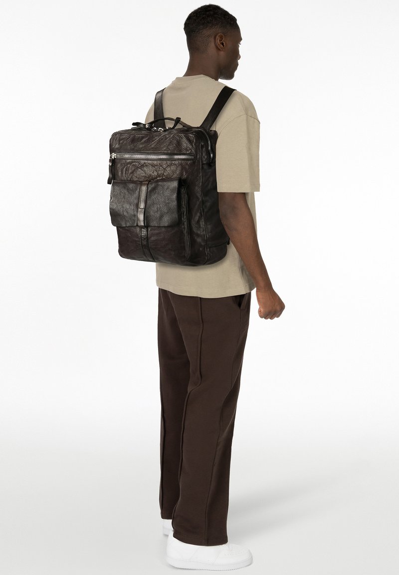 Mochila de cuero negro con superficie texturizada, múltiples compartimentos con cremallera, correas ajustables y un bolsillo frontal. Diseño limpio y minimalista.