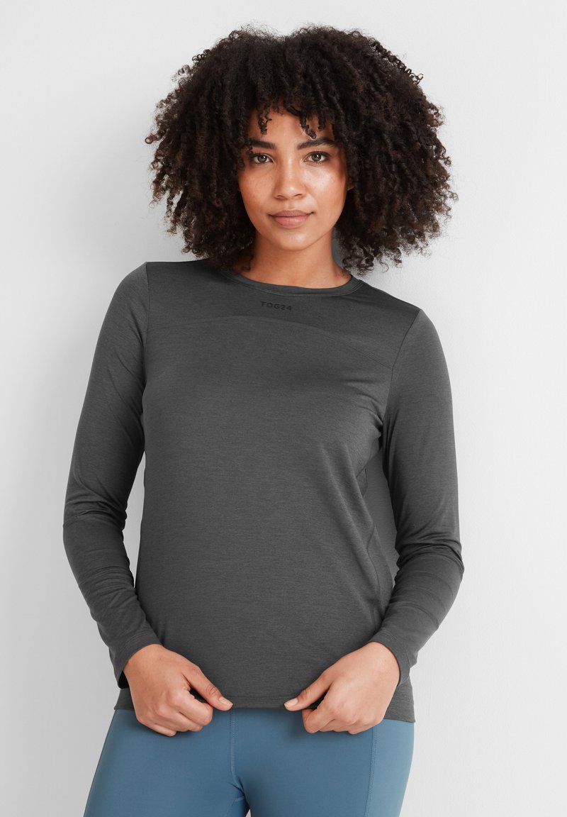 Long-sleeve athletic top in dark gray, featuring a smooth texture, round neck, and a minimalist logo near the collar. Paired with light blue leggings.