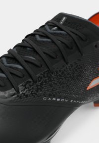 Black soccer cleat featuring a textured upper with a carbon fiber pattern and orange accents, round toe, and black laces.