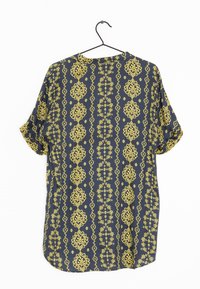 Chemise bleue à manches courtes avec un motif floral jaune, dotée d'un col rond et d'une coupe ample, suspendue à un cintre en métal noir.